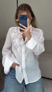 Close-up of white long sleeve shirt featuring intricate floral embroidery and buttons