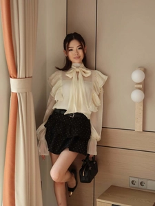 Detailed view of cream chiffon shirt with bow neck and ruffle sleeves paired with skirt