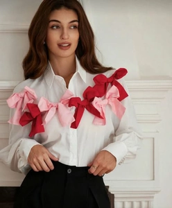 Detail of white long sleeve shirt featuring decorative pink and red oversized 3D bows