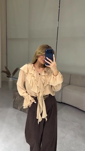Détail d'un chemisier beige à volants avec un pantalon marron à taille haute et large