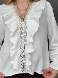 Detailed close-up of V-neck white blouse with ruffle trim and lace cut-out texture