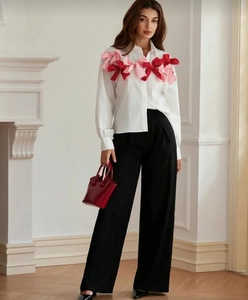 Detailed view of white long-sleeved shirt featuring 3D pink and red bow embellishments