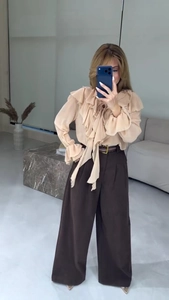 Détail du chemisier en mousseline à volants abricot et pantalon marron à jambes larges