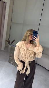 Détail du col en V à volants avec glands et manches évasées sur cette blouse abricot