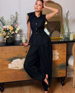 Detail view of black sleeveless vest with elegant gold embossed buttons and textured fabric