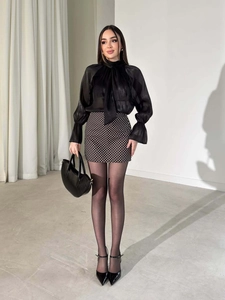 Dettaglio di elegante camicetta in chiffon nero con fiocco e gonna a pois alla moda