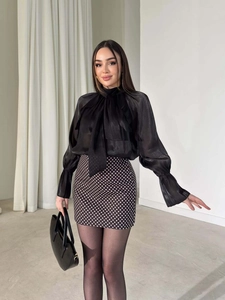 Dettaglio dell'elegante camicetta nera trasparente con fiocco e polsini elastici