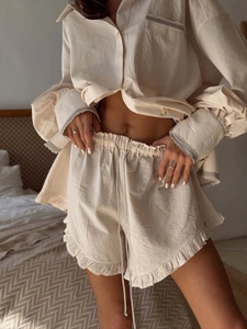 Close-up of linen shirt sleeve with fringe edge and ruffled hem shorts in warm bedroom