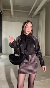 Dettaglio di elegante camicetta in organza nera con fiocco grande e gonna a pois