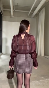 Dettaglio della camicetta in chiffon trasparente bordeaux con collo a fiocco e polsini a pieghe