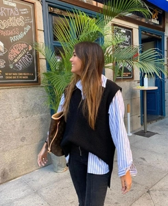 Detail of a black V-neck knit vest layered over a striped shirt for a stylish urban look