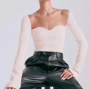 Dettaglio maglione beige a costine con scollo a cuore e pantaloni in ecopelle neri