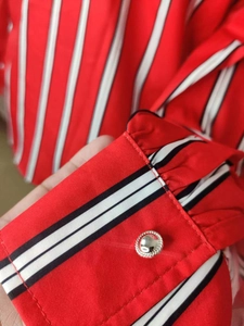 Détail d'une manche de chemise à rayures rouges avec bouton en métal et plis