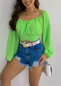 Détail du crop top vert néon à manches bouffantes avec short en jean bleu et ceinture blanche
