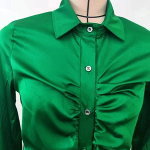 Dettaglio della camicia in raso verde smeraldo con trama arricciata e finitura lucida