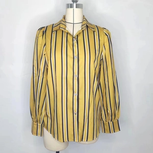 Détail d'une chemise rayée jaune moutarde avec boutons métalliques et lignes verticales
