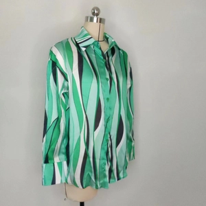 Dettaglio camicia con stampa a onde verdi che mostra il tessuto satinato e il polsino