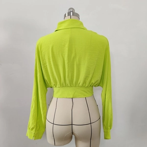 Detail of neon green cropped shirt featuring a textured fabric and cuffed long sleeves