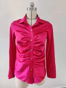 Dettaglio della camicia in raso magenta a maniche lunghe con eleganti pieghe e bottoni