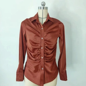 Dettaglio dell'elegante camicia in raso color rame a maniche lunghe con davanti arricciato