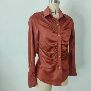 Dettaglio della camicia in raso caramello con trama arricciata e colletto classico