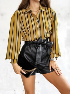 Détail de chemise à rayures jaunes avec short en cuir et pochette noire avec chaîne dorée