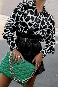 Détail d'un chemisier satiné motif girafe avec jupe en cuir noir et sac à chaîne vert
