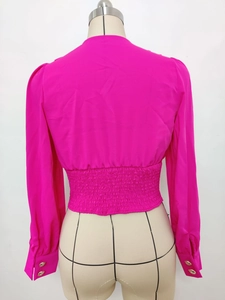 Detail view of cropped rose red blouse featuring smocked elastic waist and gold sleeve buttons
