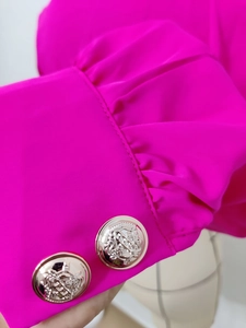 Detailed close-up of puff sleeve cuff with ornate gold crest buttons on pink satin shirt