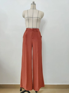 Detail of high waisted wide leg trousers in rust orange with vertical pleats and buttons