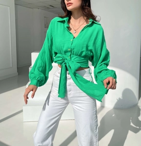 Close-up of bright green tie-front crop shirt featuring puff sleeves and textured fabric