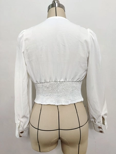 Detail view of white cropped shirt featuring smocked waist and golden decorative cuff buttons