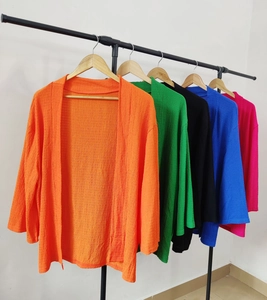 Dettaglio di cardigan leggeri in tessuto testurizzato nei colori arancio, verde e rosa