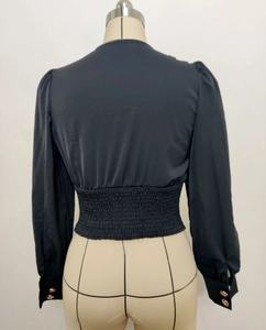 Detail of smocked elastic back and puff sleeves with gold buttons on black blouse