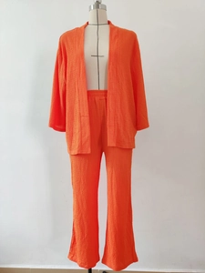 Dettaglio del completo a due pezzi arancione plissettato con cardigan e pantaloni