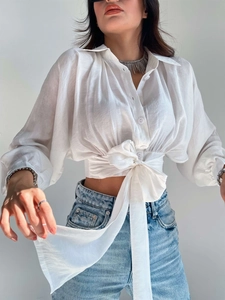 Detail of white cropped shirt featuring long batwing sleeves and large waist tie bow