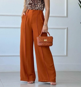 Detail of high-waisted orange-brown wide-leg trousers with textured pleated fabric