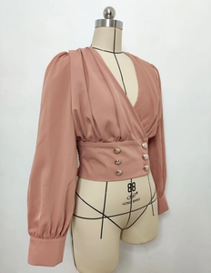 Detail of pink V-neck crop blouse featuring gold buttons and cinched waist on mannequin