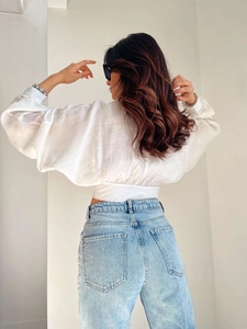 Back view of a white cropped long-sleeve tie-back shirt paired with light blue denim jeans