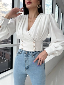 Detail of white V-neck wrap shirt featuring puffed sleeves and six gold waist buttons