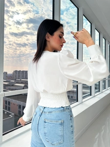 Detail of white satin long sleeve blouse featuring smocked waist and puffed sleeves