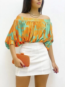 Detail of off-shoulder pleated top with orange leaf print and high waist white skirt