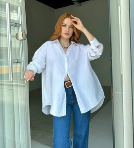 Detail of white oversized long sleeve shirt with curved hem and buttoned cuffs