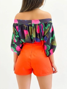 Back view of floral off-shoulder shirt paired with bright orange high-waisted shorts