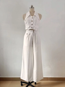 Detail of white halter neck waistcoat with amber buttons and matching wide-leg trousers