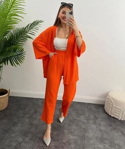 Dettaglio di un set a due pezzi arancione acceso con top plissettato e pantaloni larghi