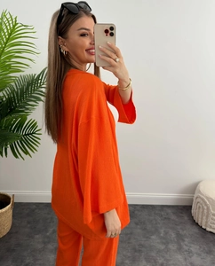 Dettaglio di un set due pezzi plissettato arancione con camicia e pantaloni lunghi