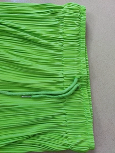 Detail of bright green pleated pants with elastic waistband and braided drawstring ties