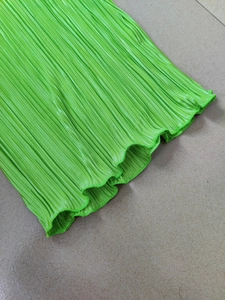 Detailed view of neon green plissé fabric featuring a vertical pleated texture and lettuce hem