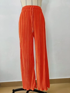 Detail view of bright orange pleated wide-leg pants featuring an elastic drawstring waist
